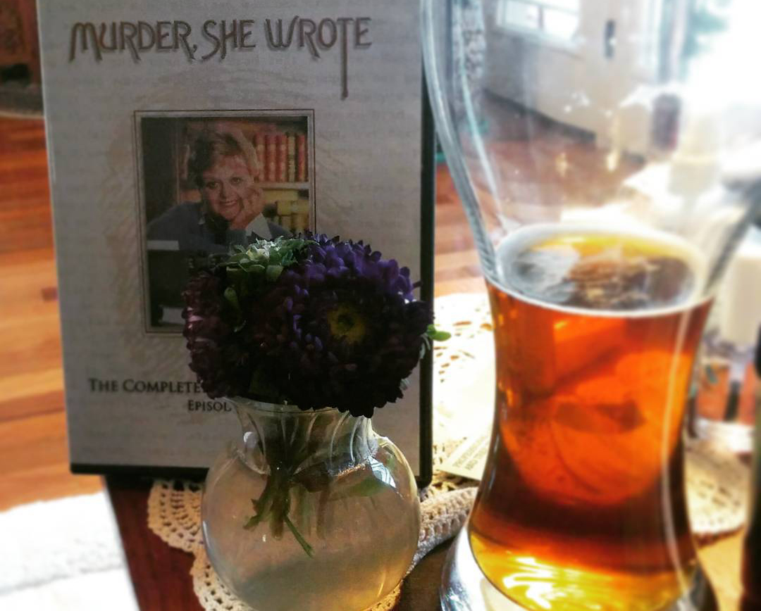 Photo of a glass of beer next to the Murder She Wrote dvds and a vase of purple flowers.